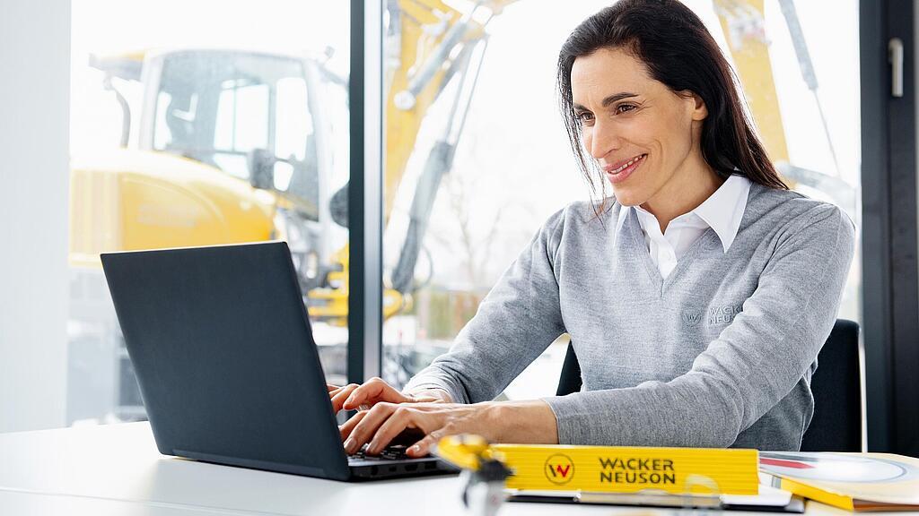 Wacker Neuson employee sitting at a laptop and smiling.