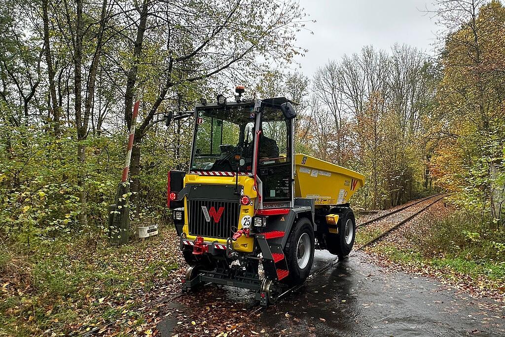 Yellow rail-road construction dumper driving on railway tracks through autumn forest on wet surface