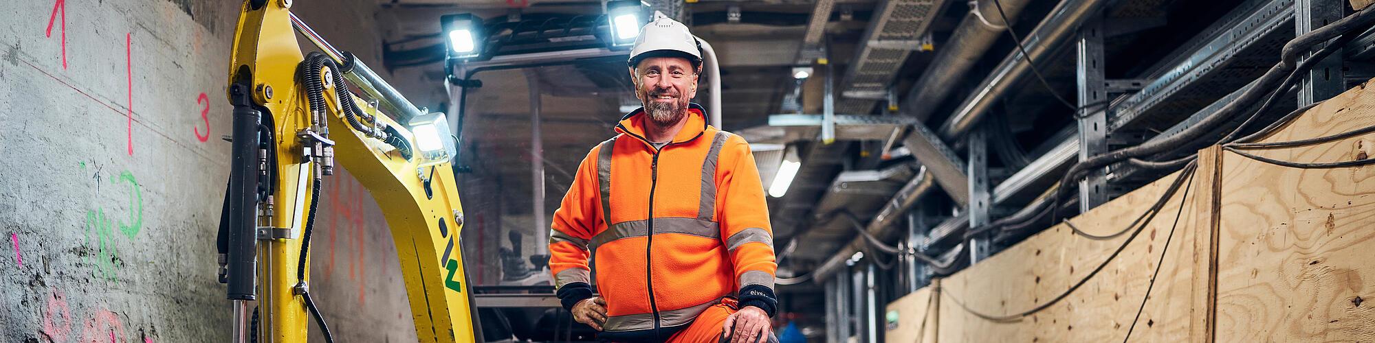 Mann, der auf einer Baustelle vor einem elektrischen Bagger steht