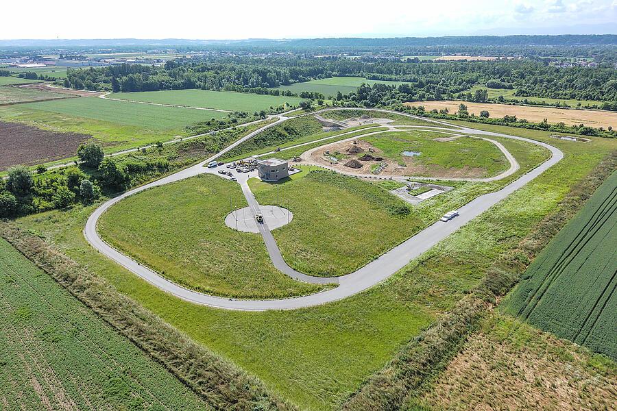 Sicht auf die Testarena in Linz mit einer asphaltierten Rundstrecke, einem Testgelände für unebene Straßen, einer Lärmmessstation und Testbereichen inmitten einer weitläufigen grünen Landschaft.