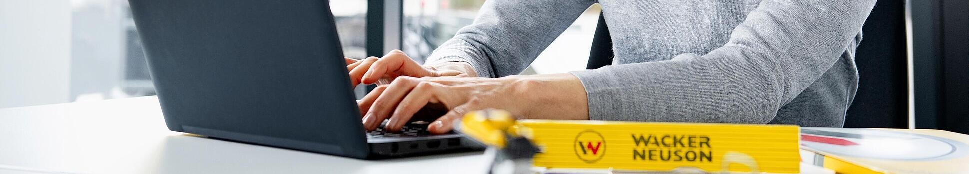 Wacker Neuson employee sitting at a laptop and smiling.