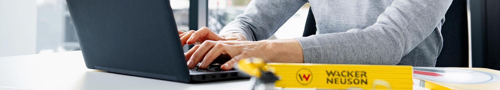 Wacker Neuson Mitarbeiterin sitzt lächelnd am Laptop.