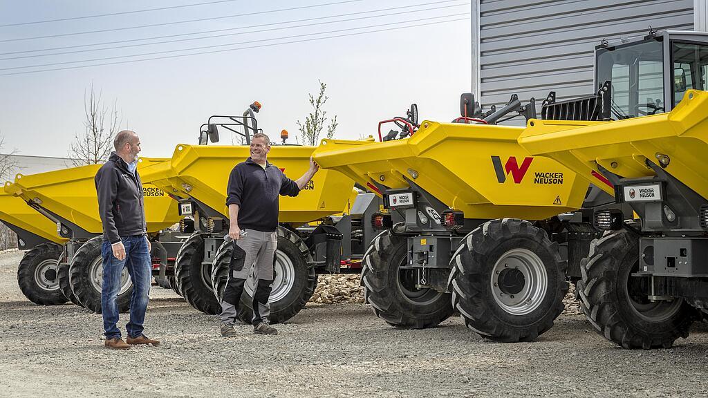 Zwei Männer stehen neben mehreren gelben Wacker-Neuson-Dumpern im Freien.