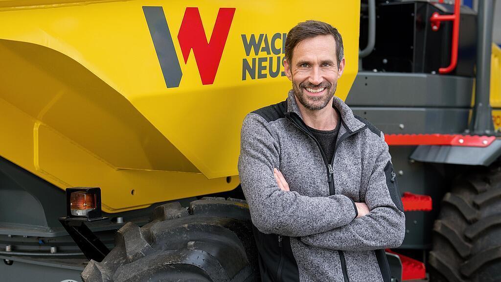 Wacker Neuson Kunde steht lächelnd mit verschränkten Armen vor einem Wacker Neuson Raddumper.