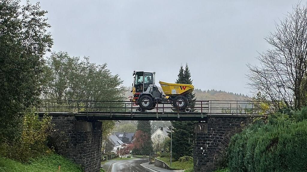 Yellow Wacker Neuson rail-road construction dumper crossing railway bridge above wet road in autumn village
