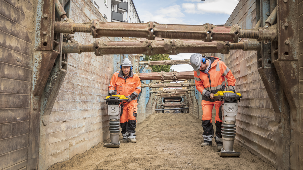 Two construction workers compact sand in a trench using Wacker Neuson rammers.