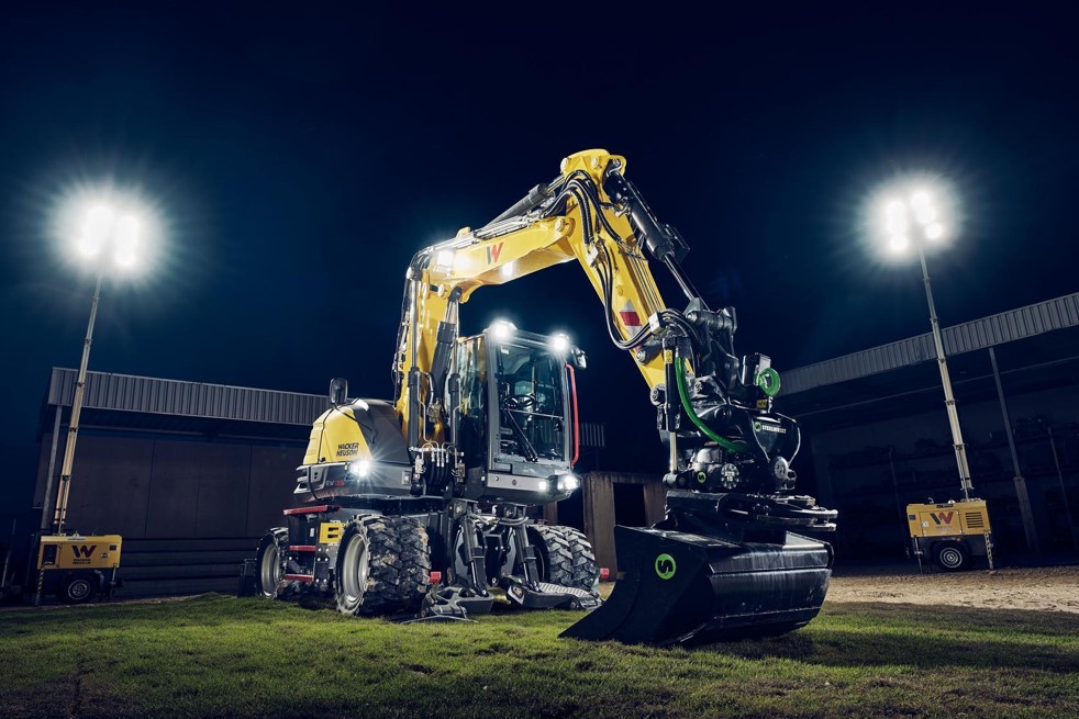 Ein Mobilbagger vom Typ Wacker Neuson EW135, ausgestattet mit einem Tiltrotator und einer Planier-Schaufel, im nächtlichen Einsatz unter Flutlicht.
